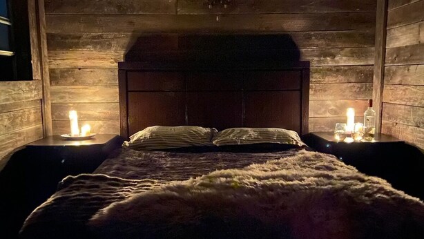 Um quarto de cabana de madeira aconchegante, com uma cama, duas mesas de cabeceira e um lustre.