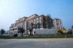 A multi-story hotel with a prominent entrance, a landscaped area with palm trees, and a clear sky. - Yueyuan International Hotel (Ningguo)