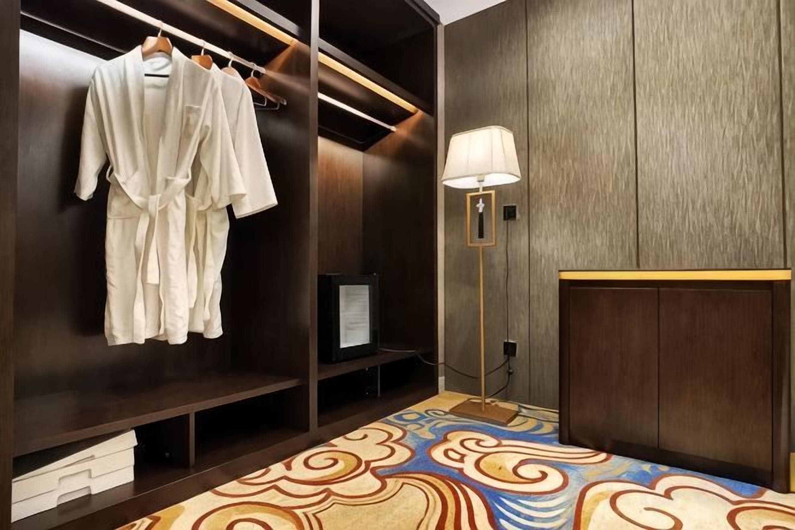 A hotel room with a walk-in closet, a bed with a patterned bedspread, a bedside lamp, and a television.