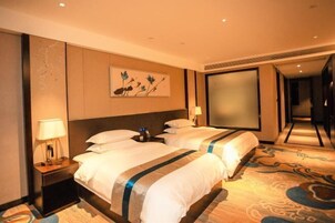 Habitación de hotel con dos camas, una mesita de noche con lámpara, un cuadro en la pared y un espejo grande.