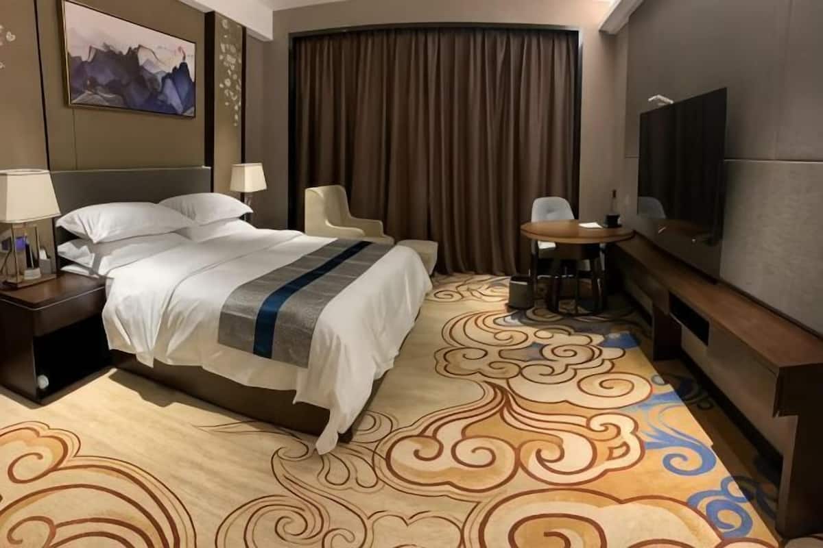 Une chambre d’hôtel équipée d’un lit, d’un bureau, d’une chaise, d’une télévision et d’une grande fenêtre avec des rideaux.
