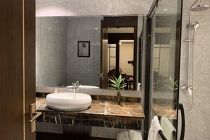 Une salle de bain moderne avec un comptoir en marbre, un lavabo blanc, un grand miroir et une cabine de douche en verre.