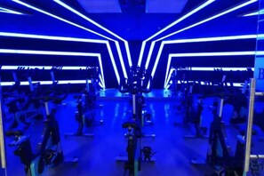 Una habitación con equipo de ejercicio, un espejo grande y un techo con luminarias lineales.