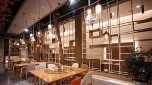 Un espace de restauration moderne avec des tables et des chaises en bois, des luminaires suspendus et une grande fenêtre donnant sur l’extérieur.