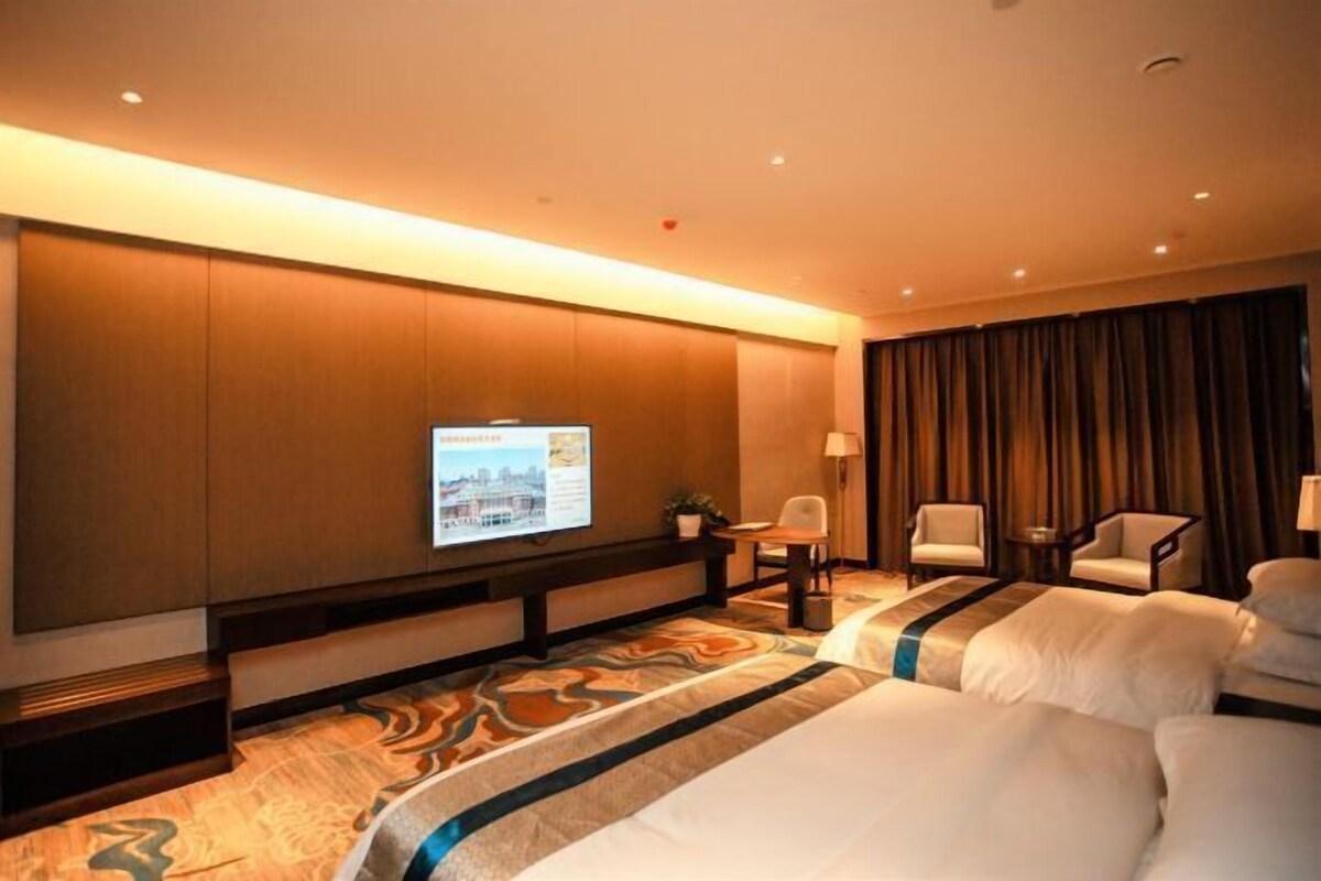 Ein Hotelzimmer mit einem großen Bett, einem an der Wand befestigten Fernseher, einem Schreibtisch mit Stuhl und Blick auf die Stadt durch das Fenster.