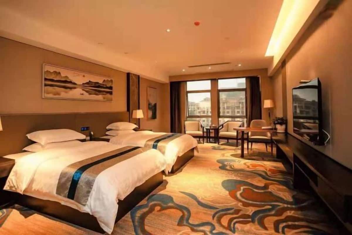 Une chambre d’hôtel avec deux lits, un coin repas, une télévision et une grande fenêtre.