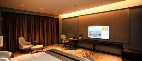A hotel room with a bed, two armchairs, a small table, a TV, and a large window with curtains.