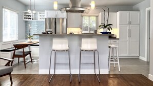 Una cocina moderna con una isla central, taburetes de bar, electrodomésticos de acero inoxidable e iluminación colgante.