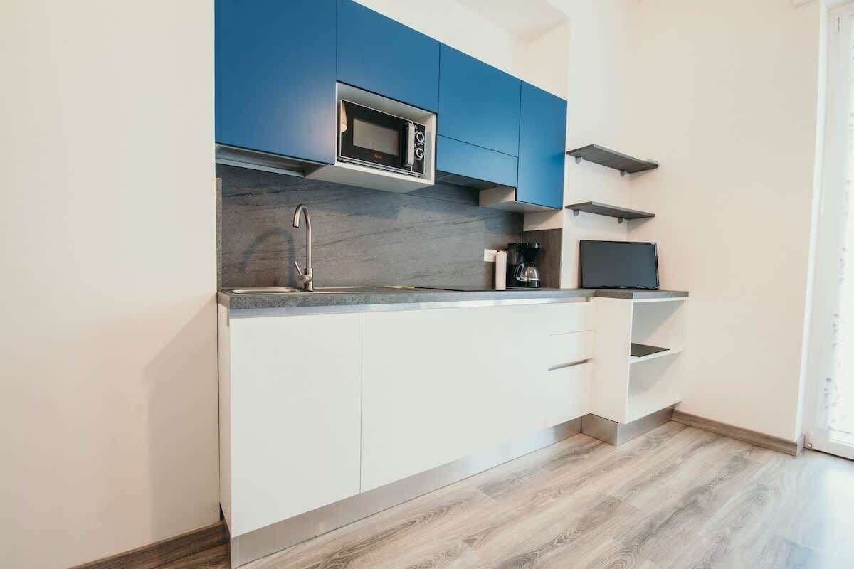 Una cocina moderna con armarios blancos, una sección superior azul, un microondas, una cafetera y un televisor en un estante.