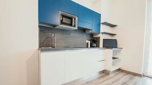 A modern kitchen with white cabinets, a blue upper section, a microwave, a coffee maker, and a TV on a shelf. - Al 13 Blu 2 - Lakeside L&b (Stresa)