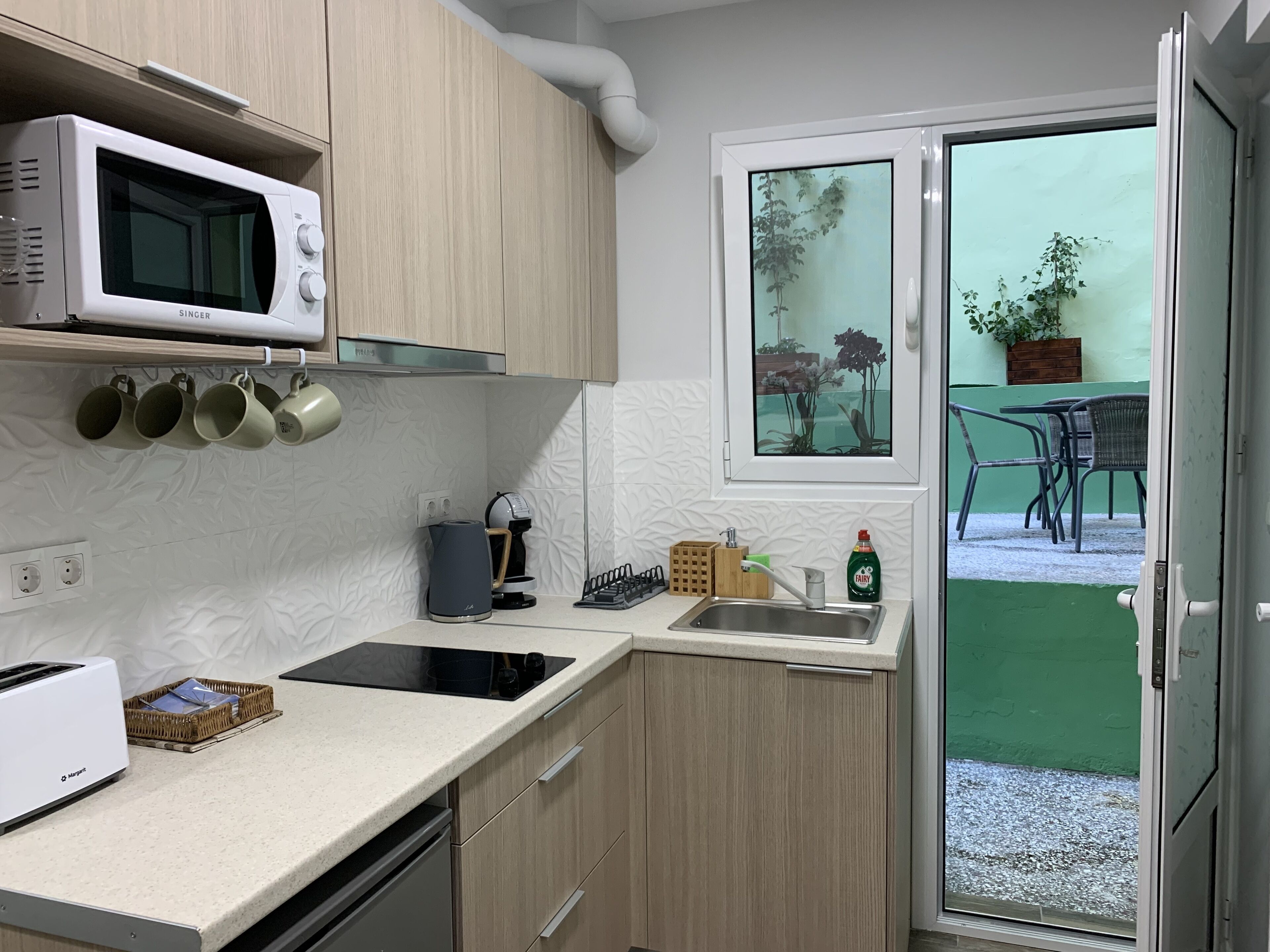 Eine moderne Küche mit Mikrowelle, Kaffeemaschine und Spüle. Ein Fenster bietet Blick ins Freie.