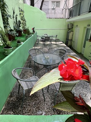 A patio with a round glass table and metal chairs, surrounded by potted plants and a green wall. - Central area of Athens, two bedroom Cozy Apartment with garden and terrace (Athina)
