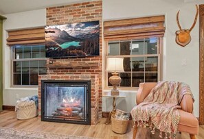 Cozy living room with a fireplace, sofa, and TV, offering a view of the outdoors.