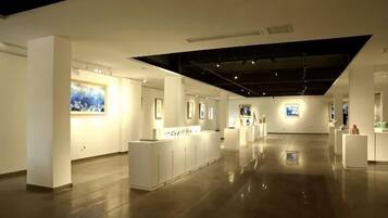 Una amplia galería con paredes blancas y suelo pulido, que presenta varias exhibiciones de arte y un elemento de iluminación central.