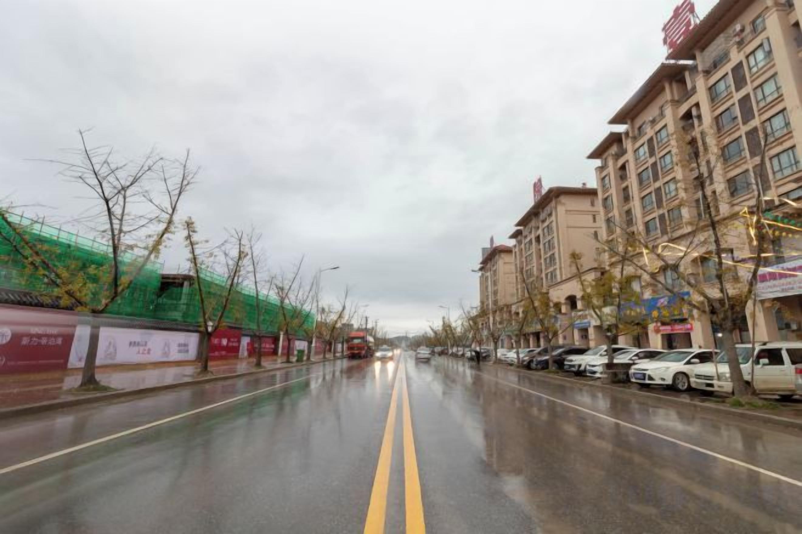 Una calle mojada en la ciudad con coches aparcados y edificios a ambos lados.