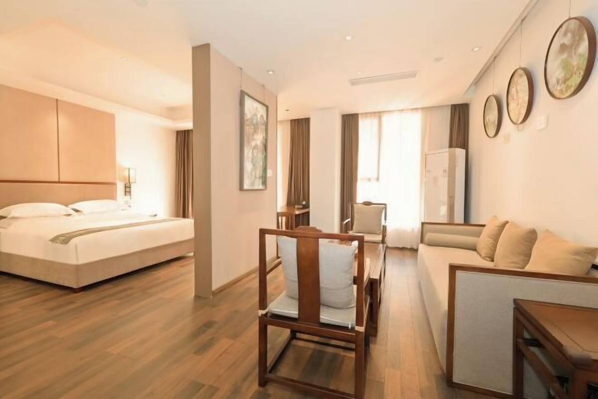 A hotel room with a bed, a wooden chair, a sofa, a dining table, and a wall with framed pictures.