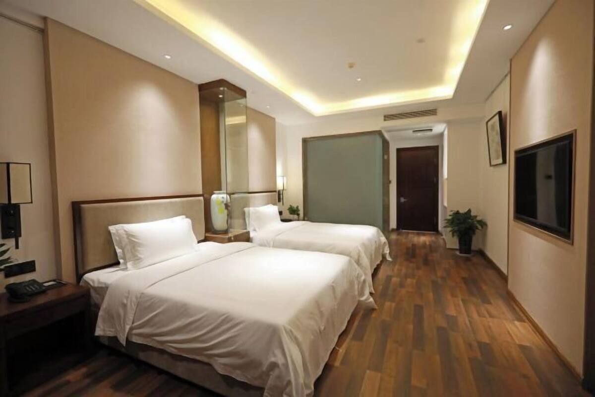A hotel room with two beds, a large mirror, a TV, and a wooden floor.