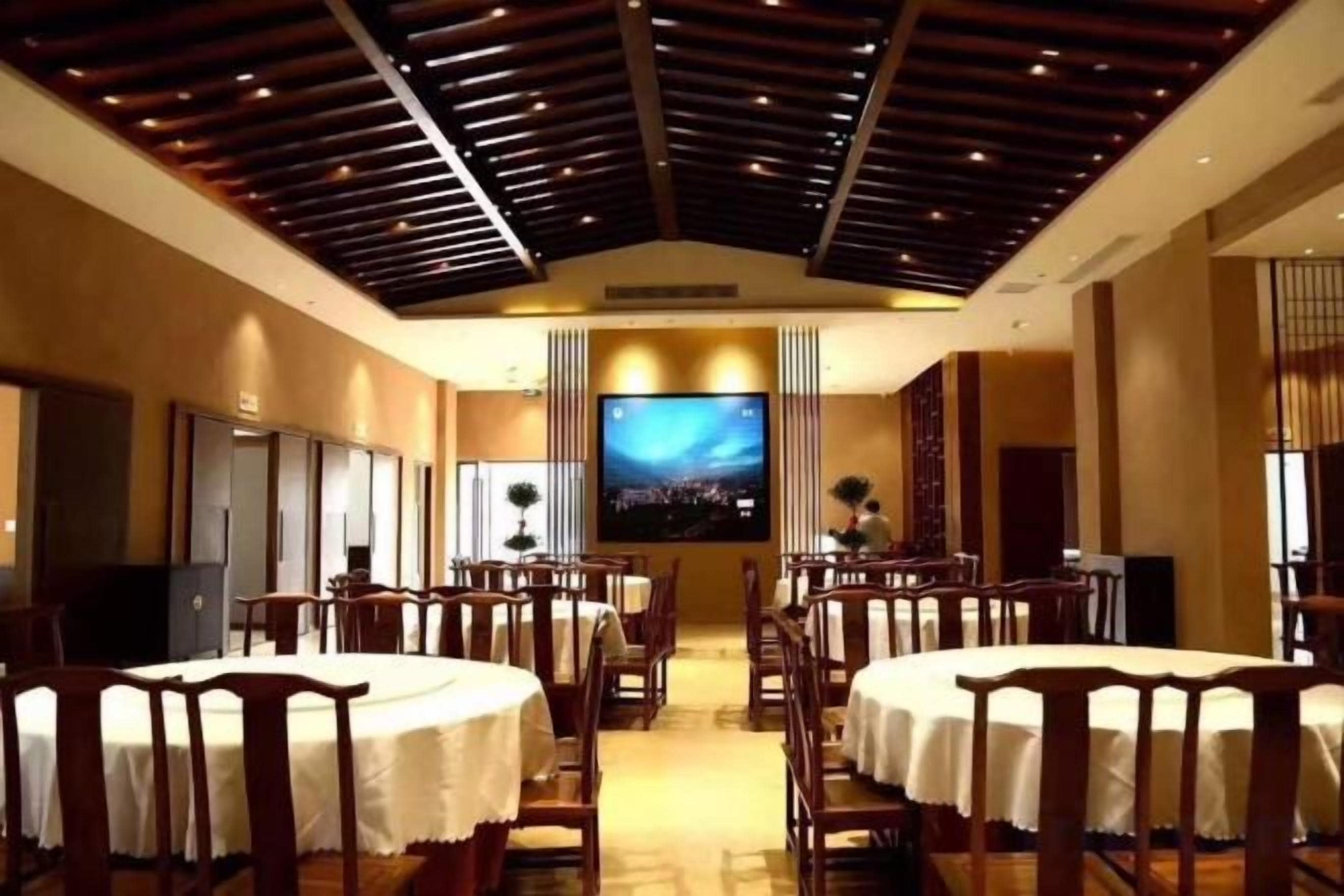 Un salón de conferencias con mesas redondas, sillas, una pantalla grande y techo de madera.
