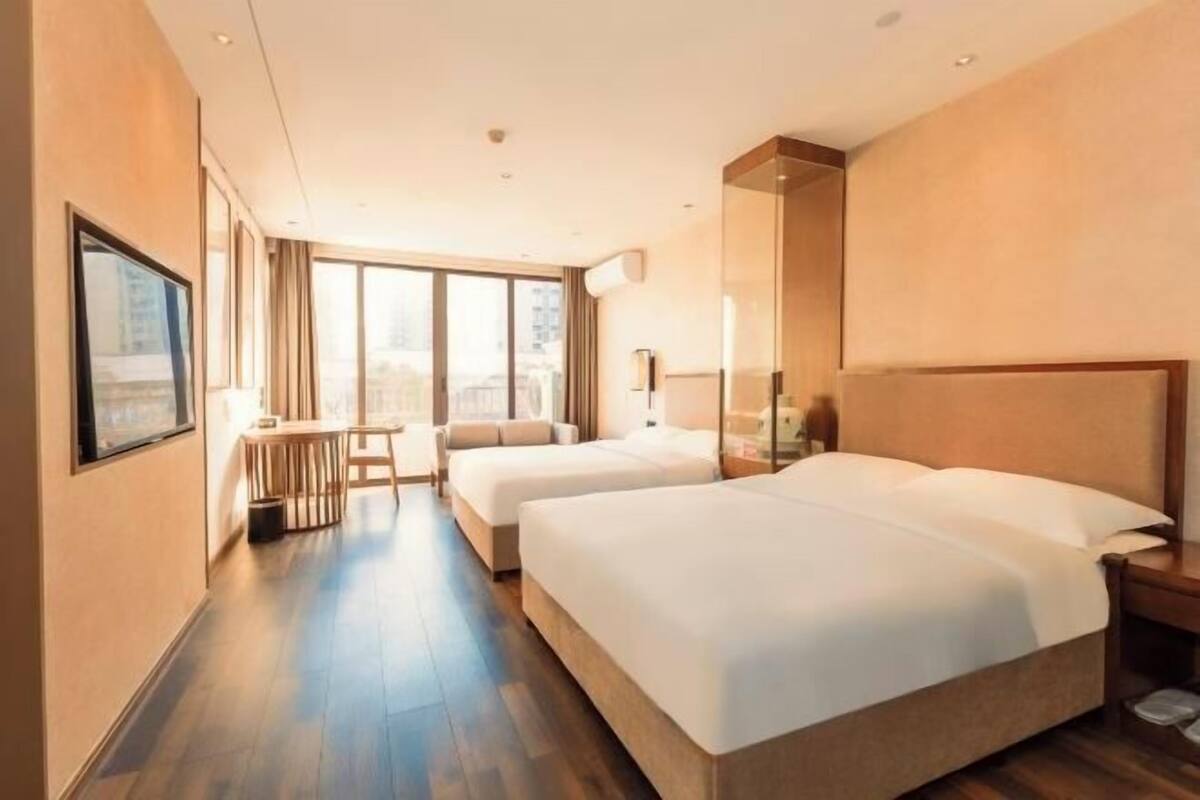A hotel room with two beds, a small table, and a large window.