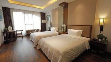A hotel room with two beds, a desk, a chair, a large mirror, and a bedside table with a lamp.