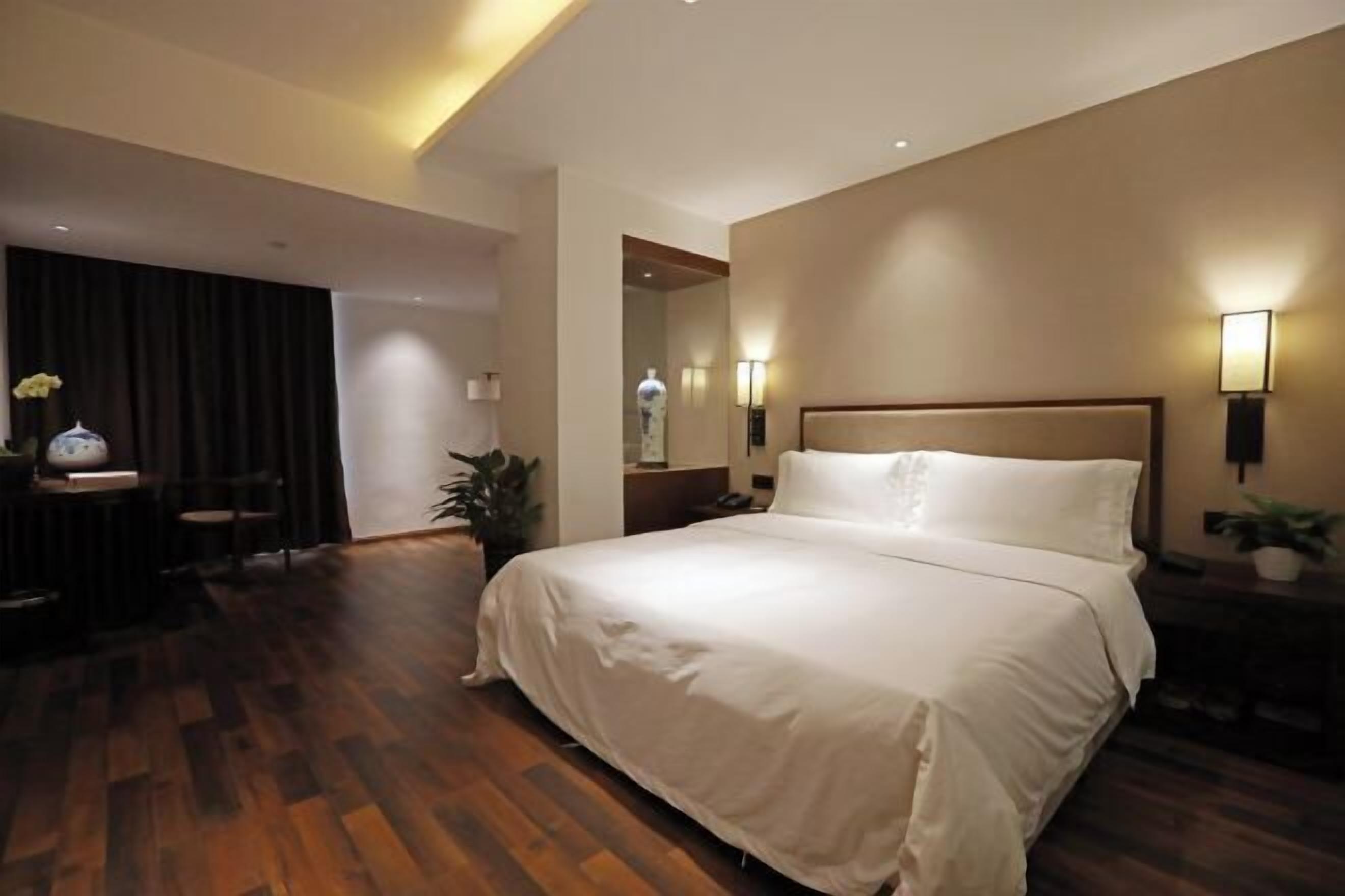 A hotel room with a large bed, a desk with a chair, and a mirror.