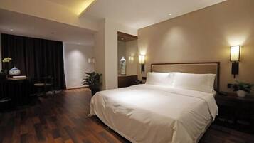 A hotel room with a large bed, a desk with a chair, and a mirror.