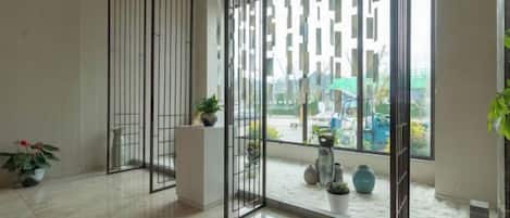 A hotel lobby with a large glass door, potted plants, and a tiled floor.