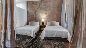 Een kamer met twee bedden, een bakstenen muur, een klein tafeltje met een lamp en een kamerbreed tapijt met dessin.