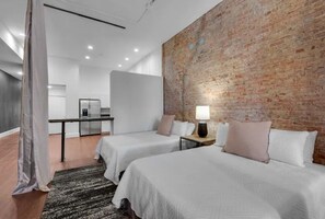 A hotel room with two beds, a brick wall, a modern kitchen area, and a large window.