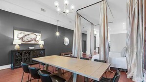 Een moderne hotelkamer met een groot bed, een zithoek met een tafel en stoelen, een kitchenette en een groot raam met gordijnen.