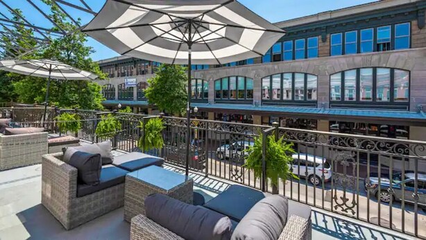Een terras met rieten meubels en parasols, met uitzicht op een straat met auto's en gebouwen.