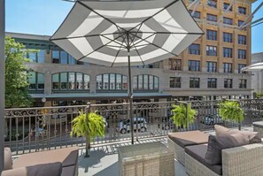 A balcony with wicker furniture, an umbrella, and a view of a building with multiple windows and balconies. - Fabu Posh B ~ Luxe Historic Palafox Balcony 1 BR (Pensacola)
