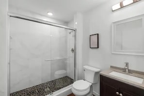 A bathroom with a glass shower enclosure, a toilet, and a vanity with a mirror.