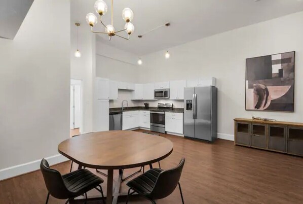 A modern kitchen with white cabinets, stainless steel appliances, and a wooden dining table with chairs.