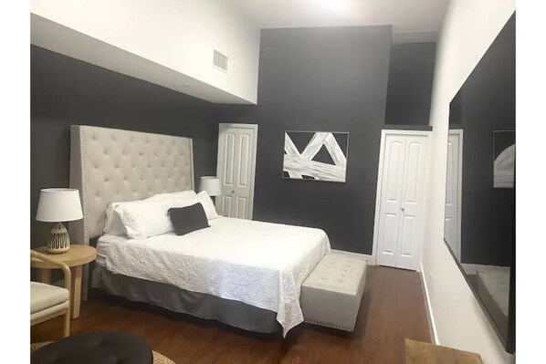 Relax in a serene bedroom with a large tufted headboard bed, bedside table, and comfortable chair.