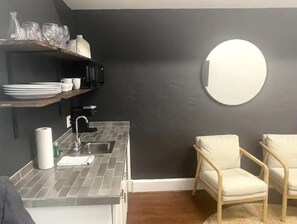 Compact kitchen with modern design, featuring a grey tiled countertop, stainless steel sink, and small range hood.