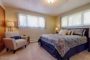 Cozy retreat with a large bed, chair, and table, featuring a patterned bedspread and a lamp.