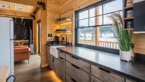 A modern kitchen with wooden cabinetry, a large window, and a view of a snowy landscape. - Clydesdale Outpost (Whitefish)