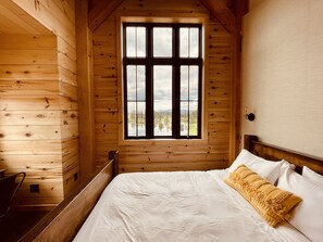 Une chambre dans un chalet en bois, avec un lit, une fenêtre donnant sur un lac et des montagnes, et une tête de lit en bois.