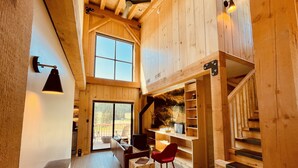 A spacious loft-style room with a large window, a wooden staircase, and a cozy seating area with a red chair. - Clydesdale Outpost (Whitefish)