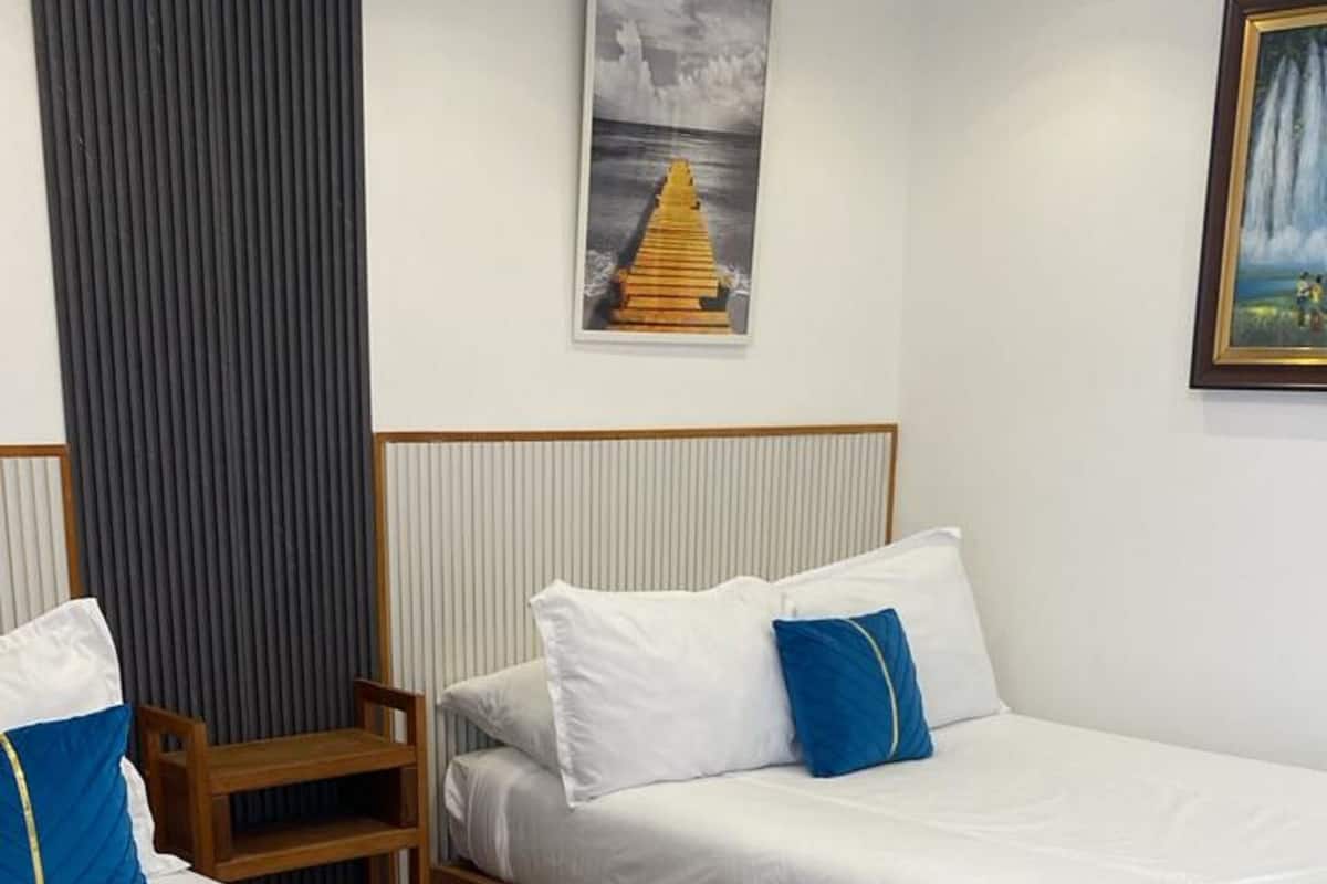 Habitación de hotel con dos camas individuales, cabecero de madera, una mesita pequeña de madera y una cortina gris.