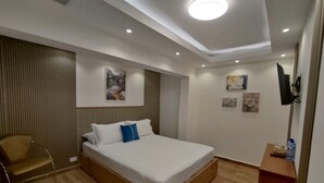 A modern bedroom with a large bed, a chair, and a flat-screen TV mounted on the wall.