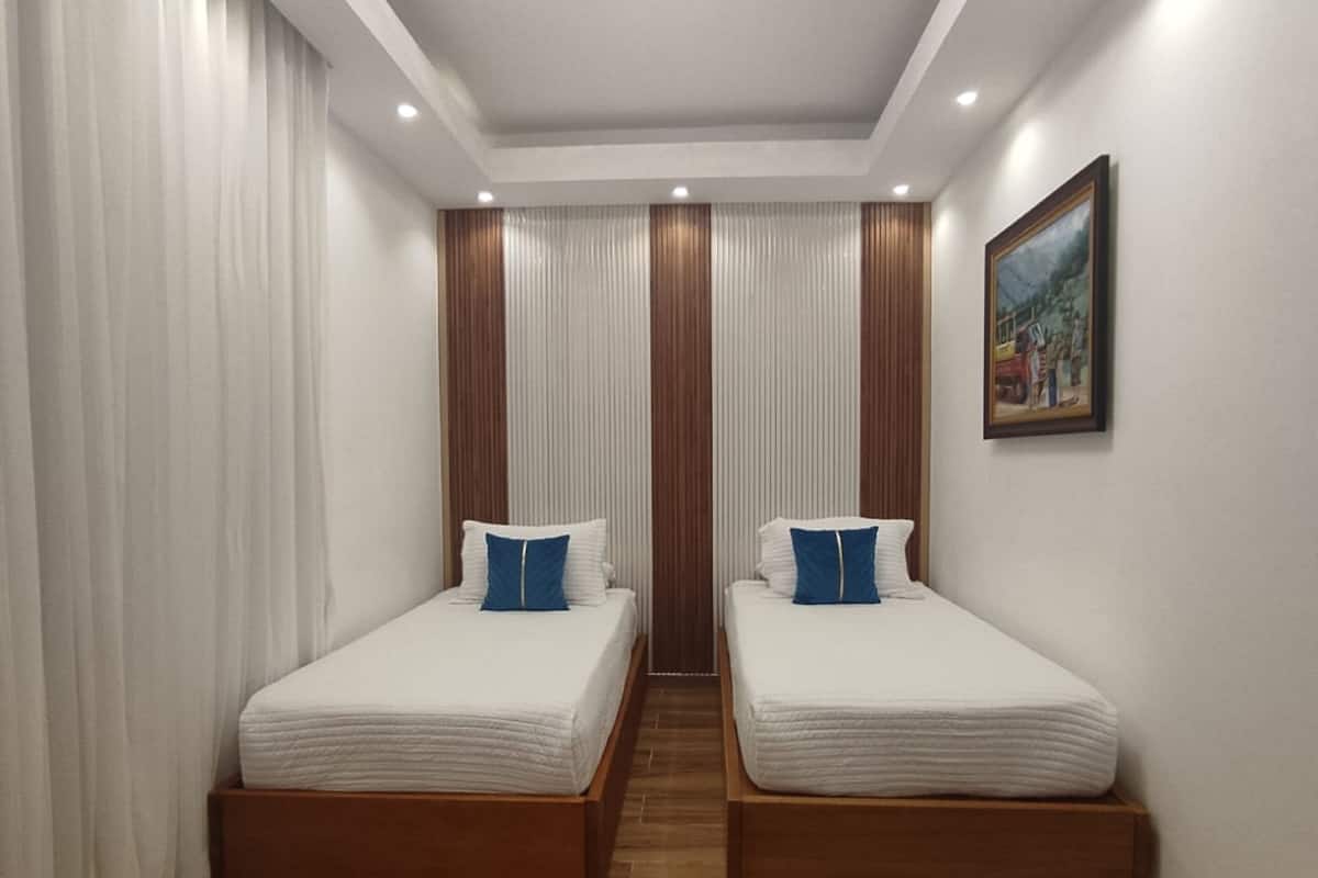 Una habitación de hotel moderna con dos camas individuales, suelo de madera, paredes blancas y una lámpara en el techo.