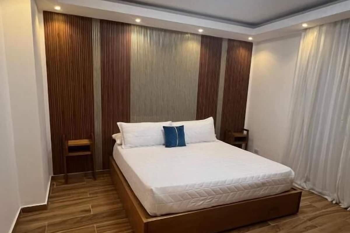 Una habitación de hotel moderna con una cama grande, paneles de madera y una lámpara en el techo.