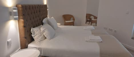A neatly made bed with white linens and pillows, a round white side table, and a wooden headboard.