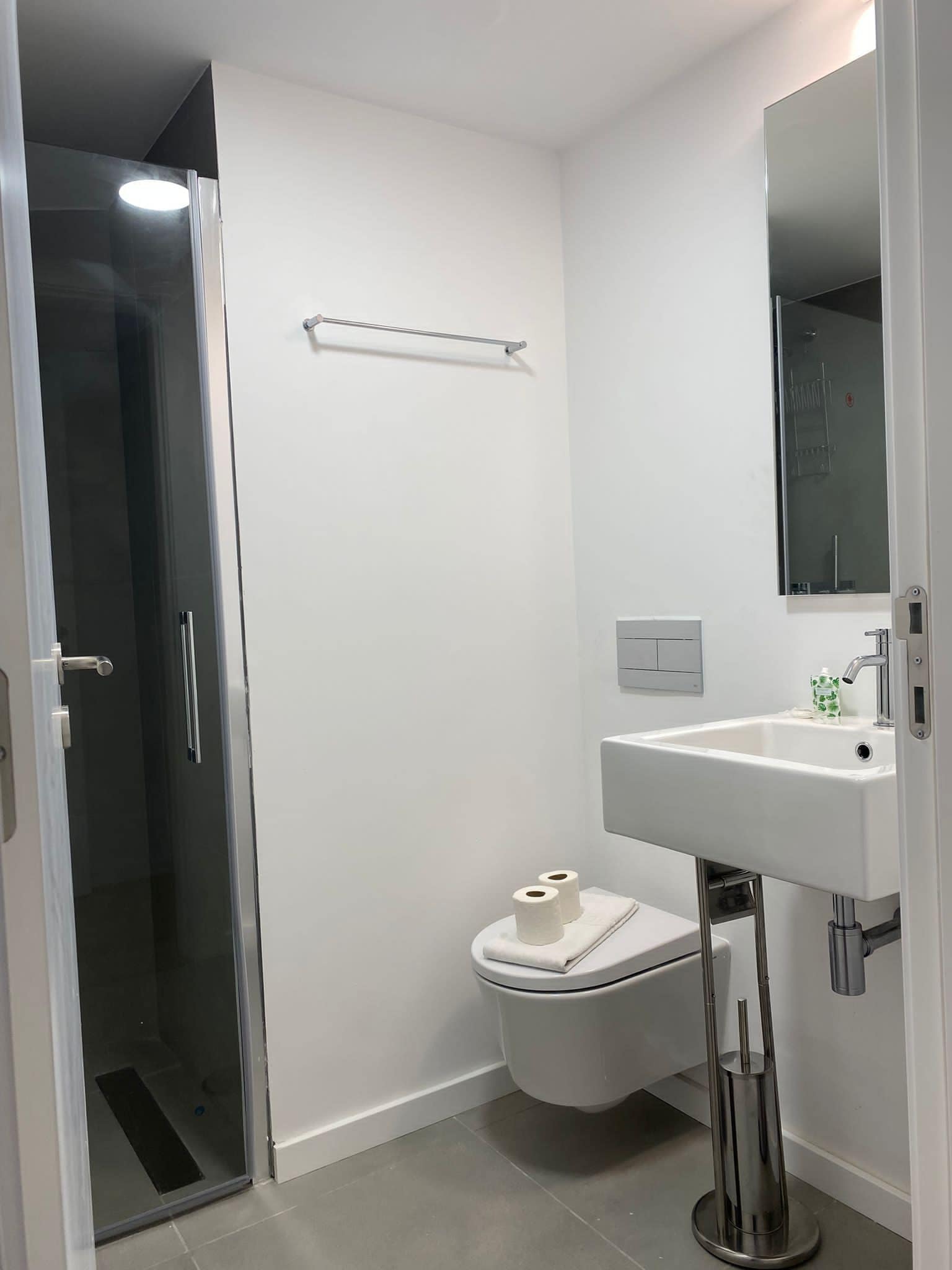 A modern bathroom with a glass shower enclosure, a white toilet, a sink with a mirror, and a towel rack.