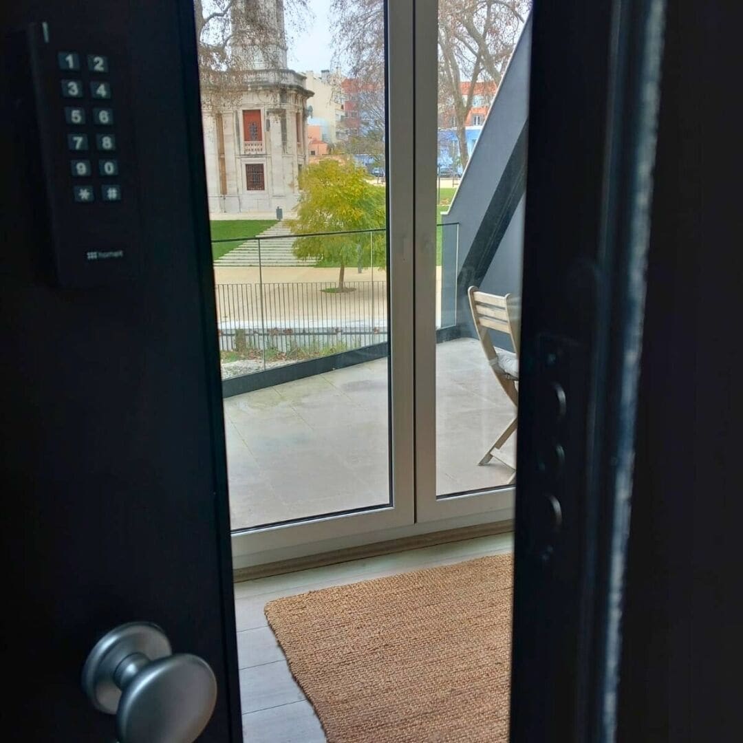 A view through a glass door with a keypad lock, a small rug, and a bench outside.