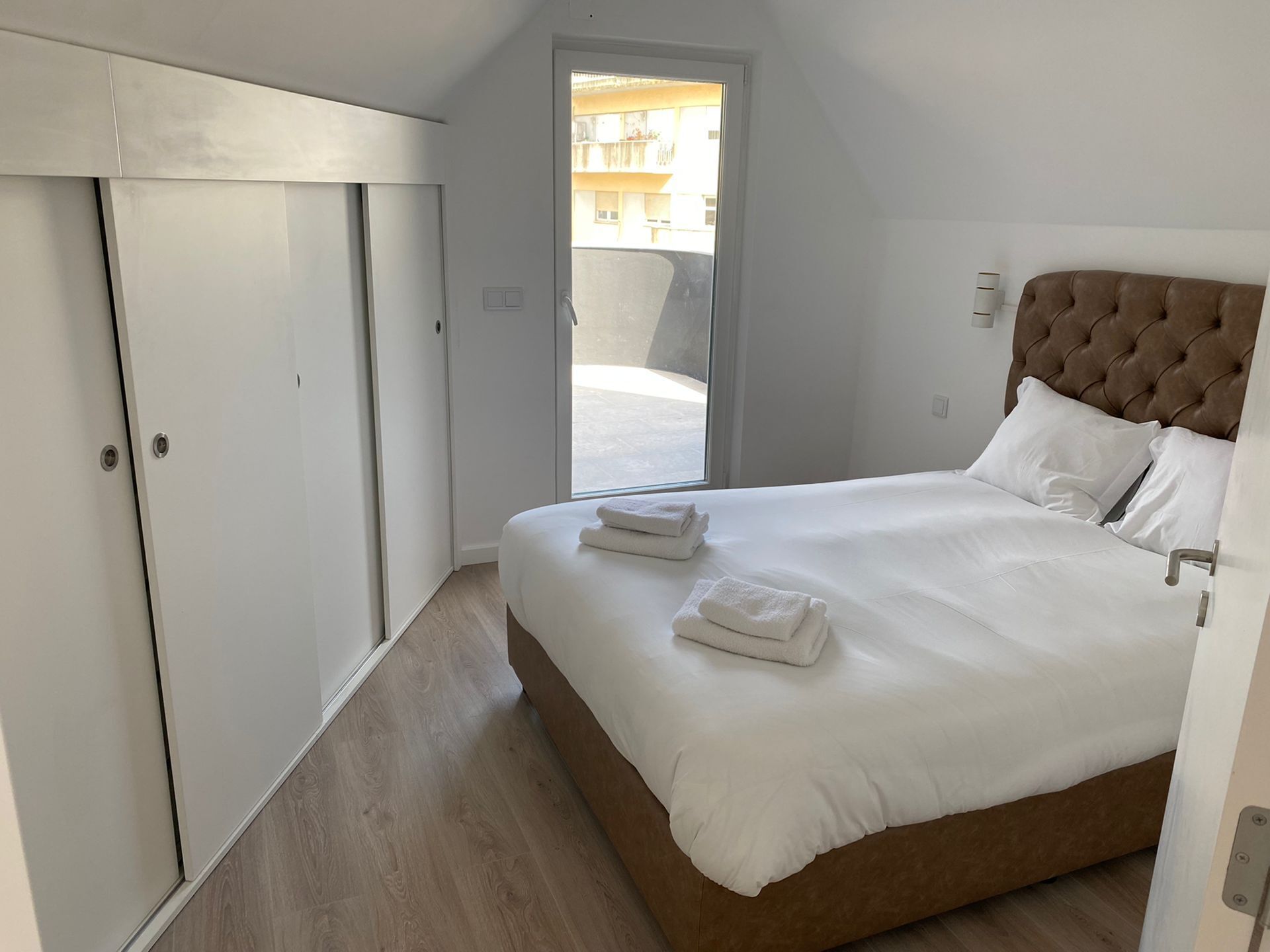 A bedroom with a large bed, white bedding, a brown headboard, and a wooden floor.
