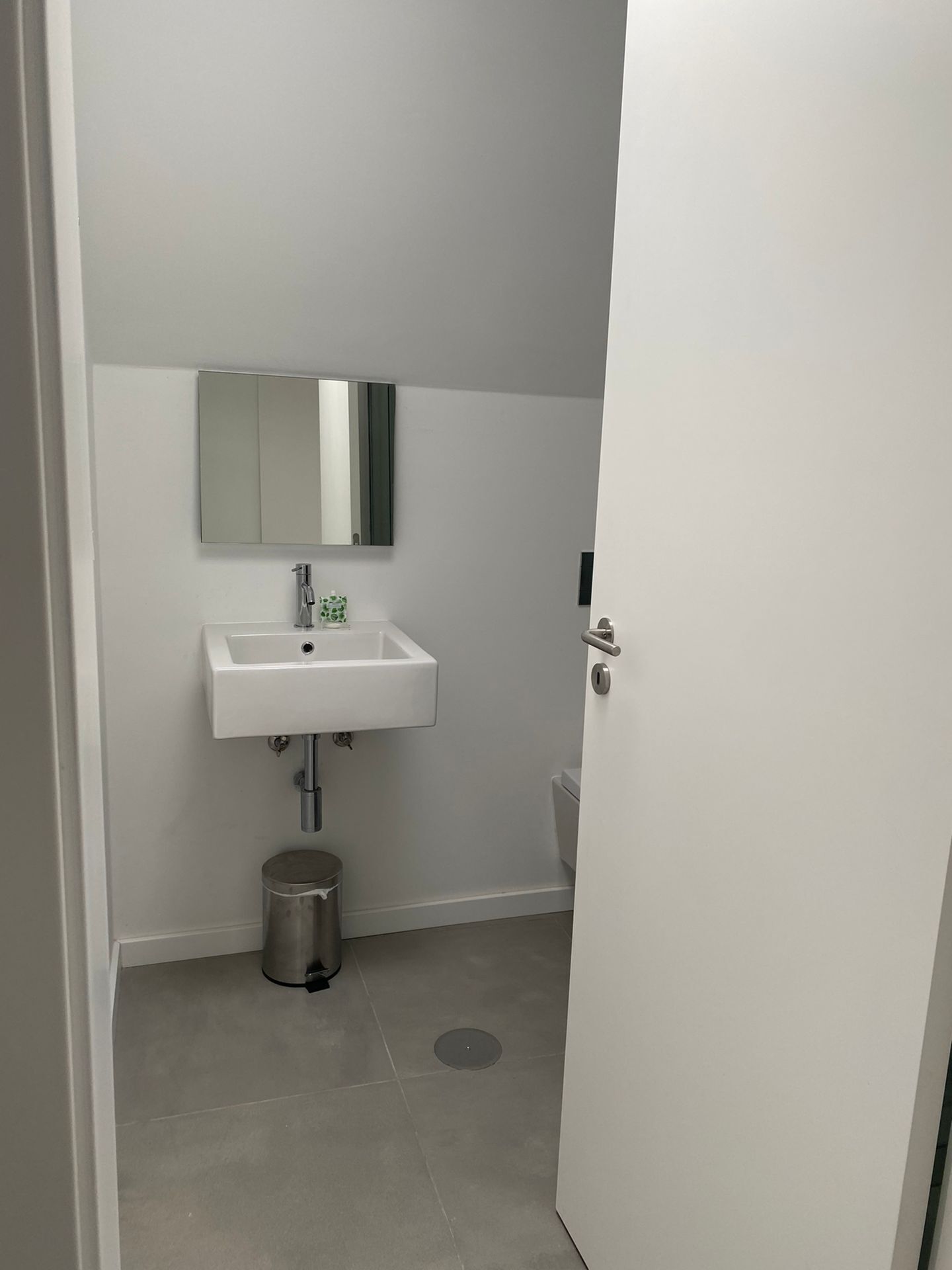 A small bathroom with a white sink, a mirror above it, and a trash can.
