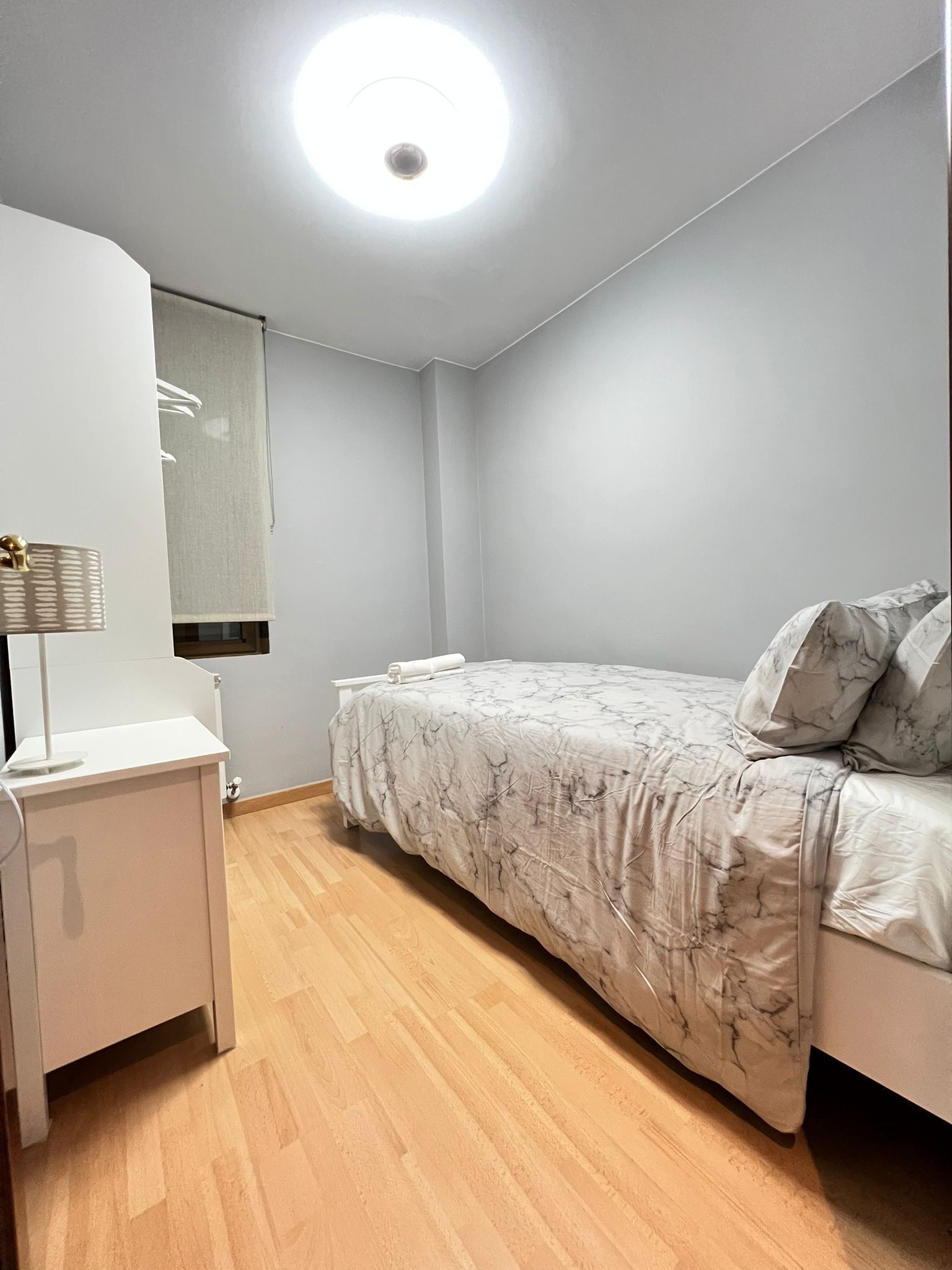 Un dormitorio con cama, mesita de noche, espejo y luz de techo.